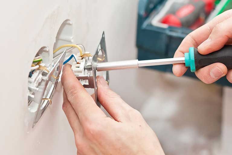 Pessoa usando uma chave de fenda para parafusar o suporte de uma tomada em uma caixa de parede branca