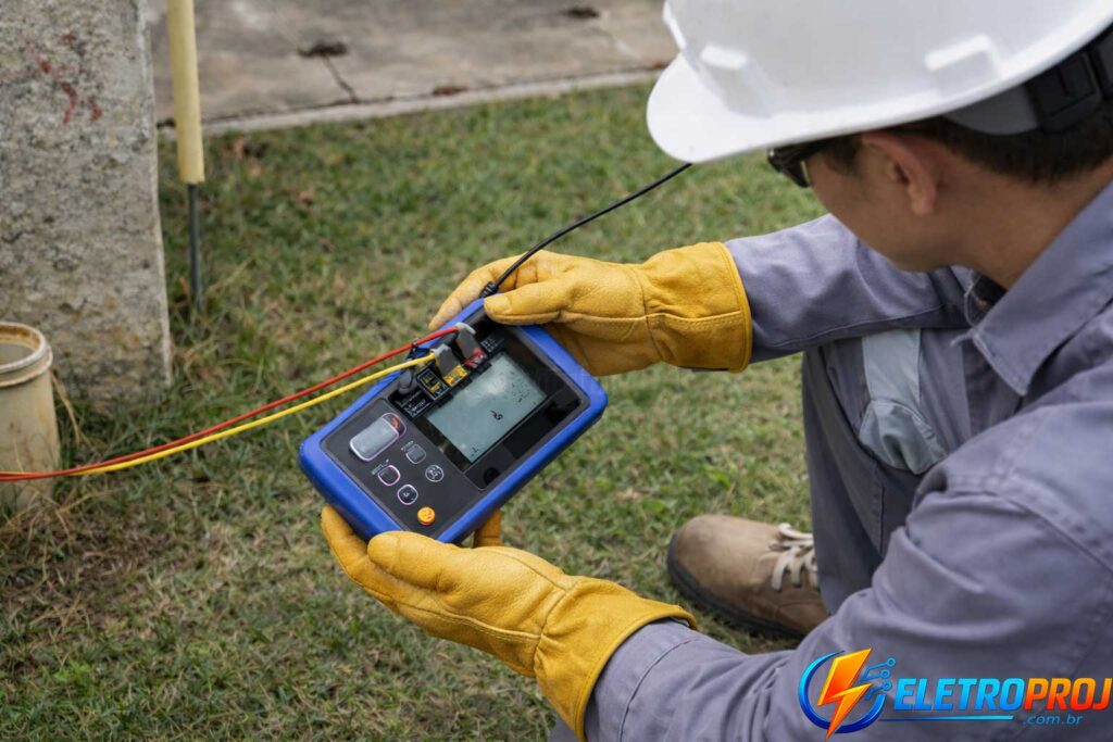 Engenheiro eletricista realizando medição de resistência de aterramento com terrômetro digital em área externa, utilizando EPIs como capacete e luvas de proteção. Manutenção de Para-Raios